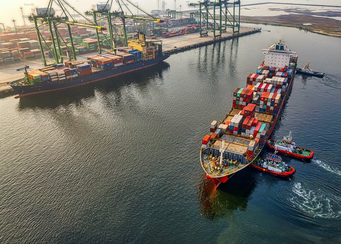 Aerial view of a container ship guided by tugboats at a port terminal